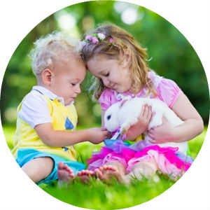 2 Children Sitting on the Grass Holding a White Bunny